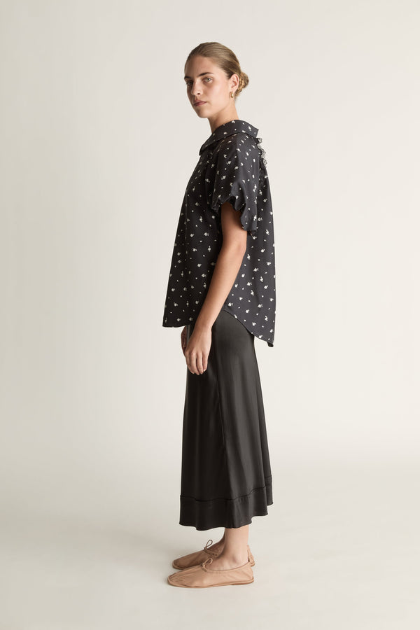 Woman wearing a black patterned blouse and black skirt on a white background