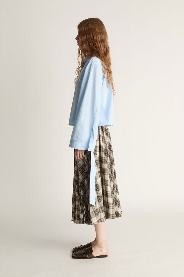 Woman wearing a light blue shirt and plaid skirt on a plain background