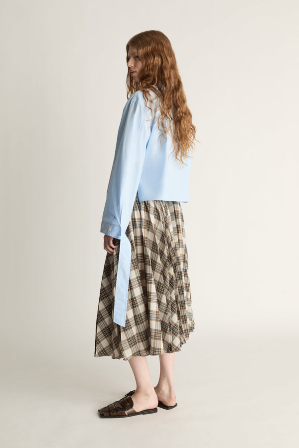 Woman wearing a light blue shirt and plaid skirt on a plain background