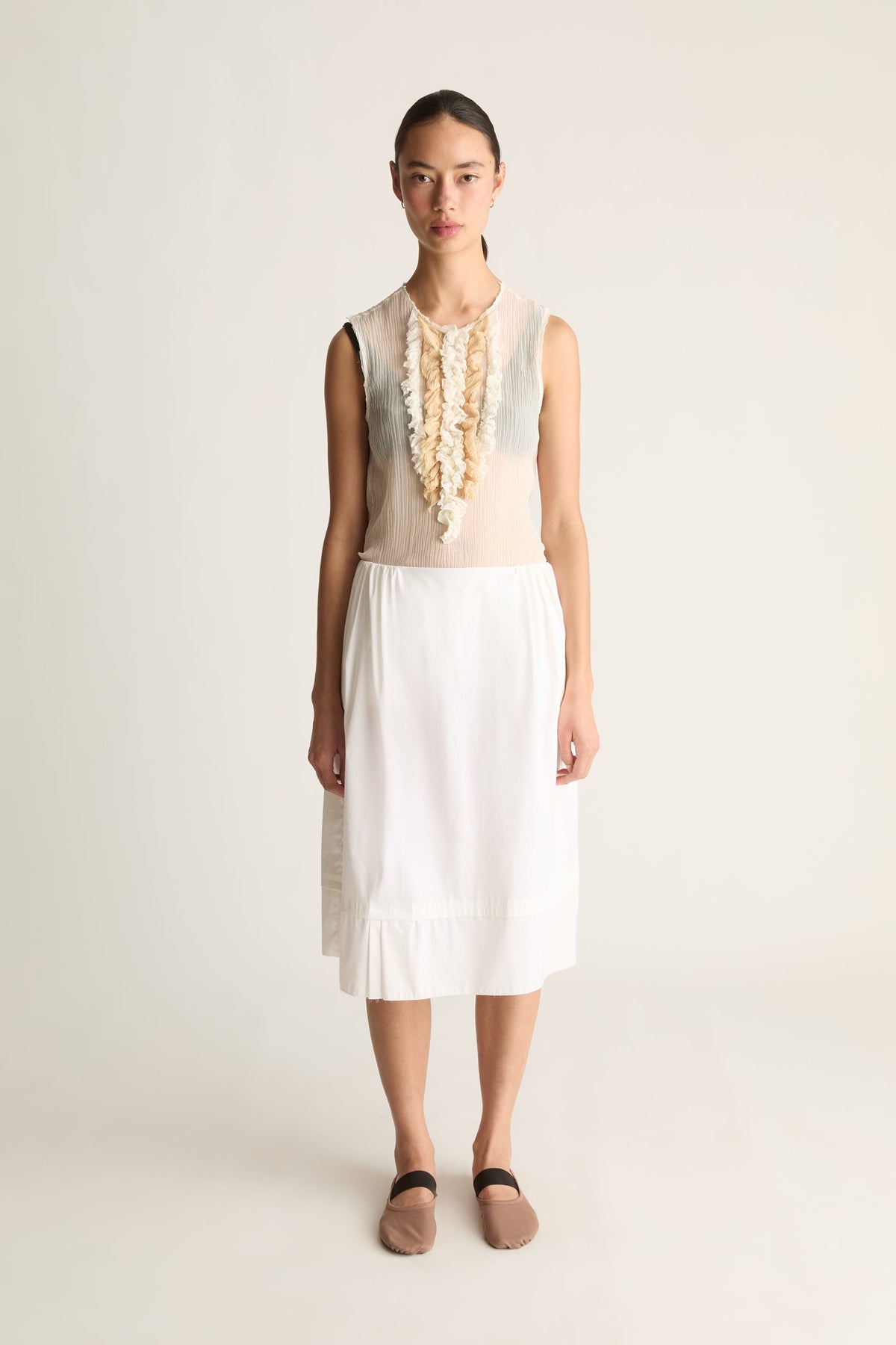 Front view of a woman wearing a white tiered midi skirt and sheer ruffle top against a white studio background