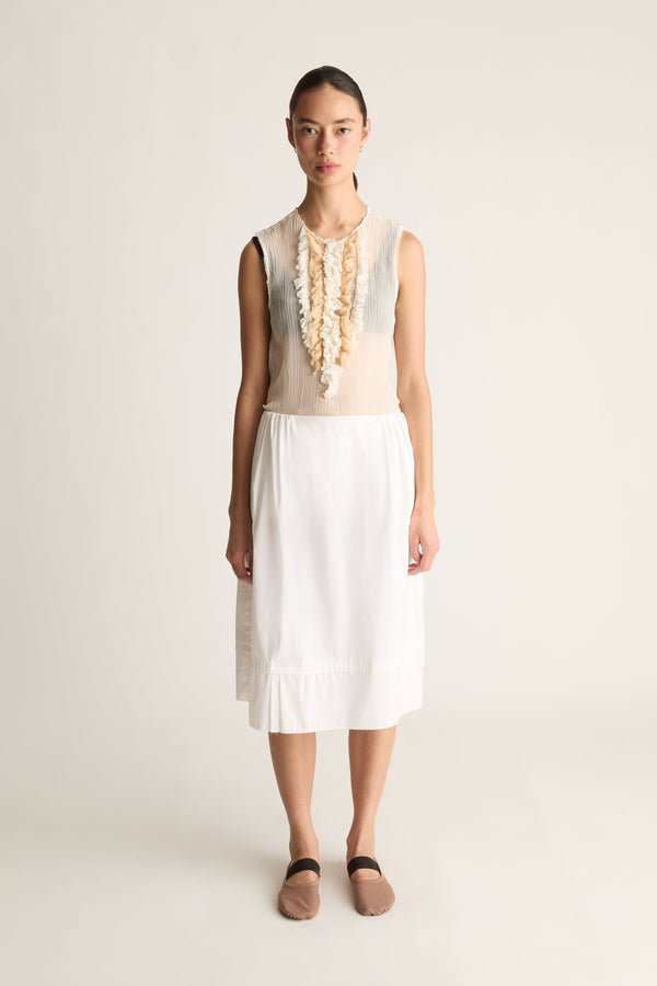 Front view of a woman wearing a white tiered midi skirt and sheer ruffle top against a white studio background