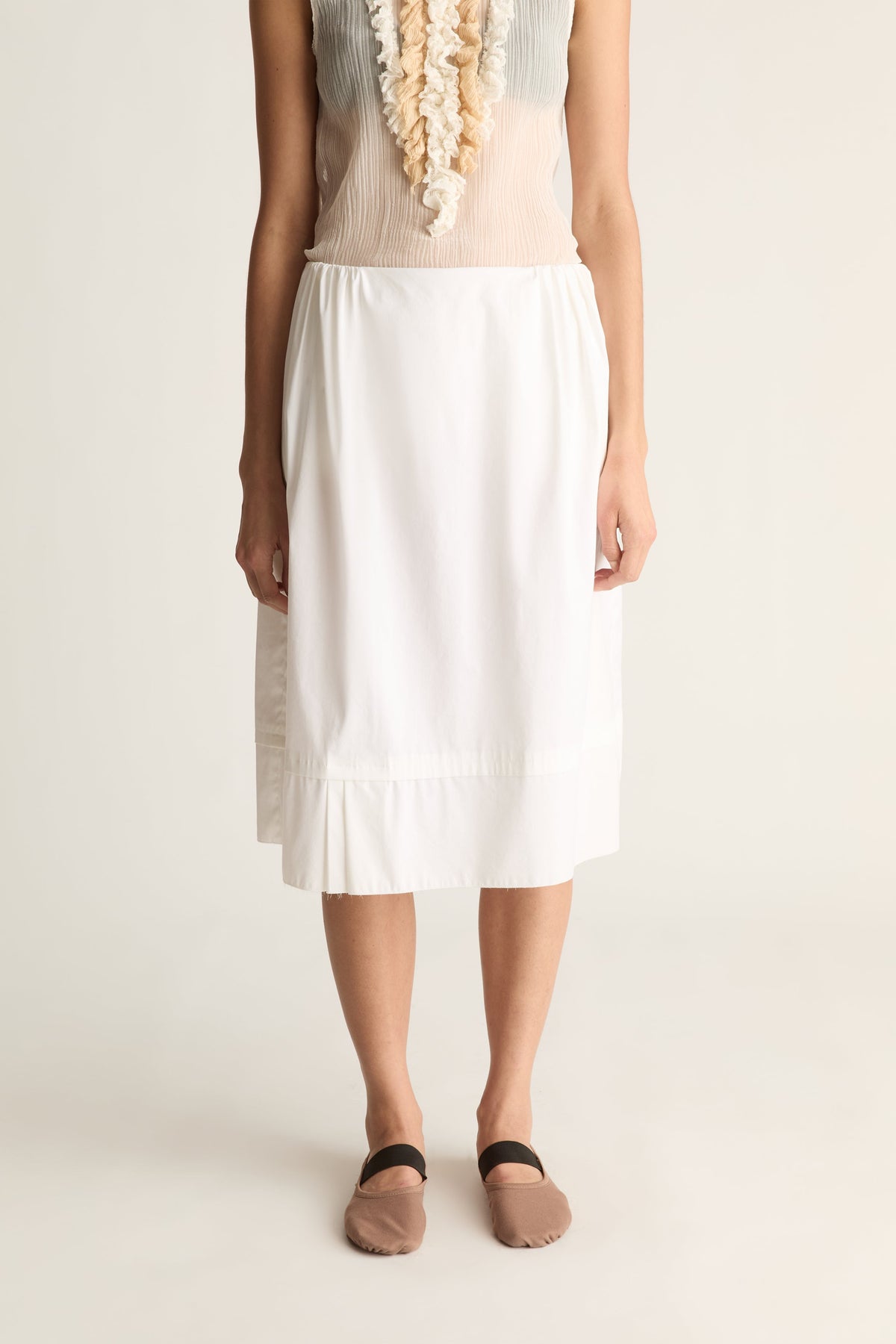 Close-up of a white elastic-waist midi skirt with a pleated hem, worn with taupe ballet flats