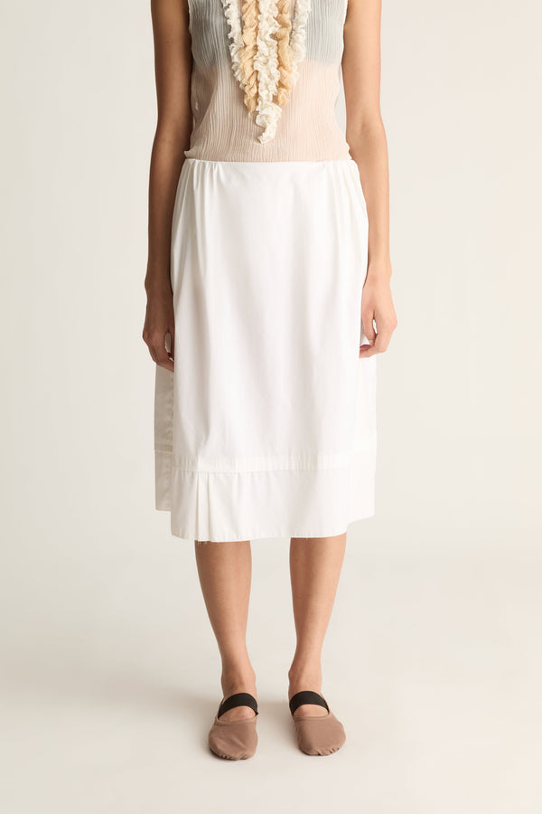 Close-up of a white elastic-waist midi skirt with a pleated hem, worn with taupe ballet flats