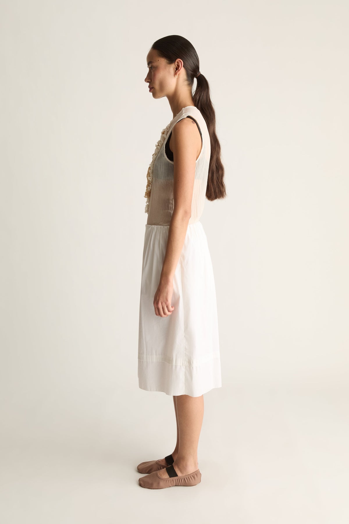 Side view of a woman with a ponytail in a white gathered midi skirt with deep hem band and a sleeveless top