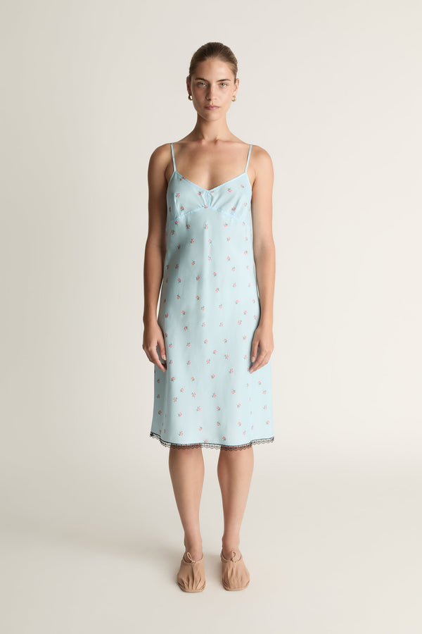 Woman wearing a light blue slip dress with a subtle pattern on a plain background
