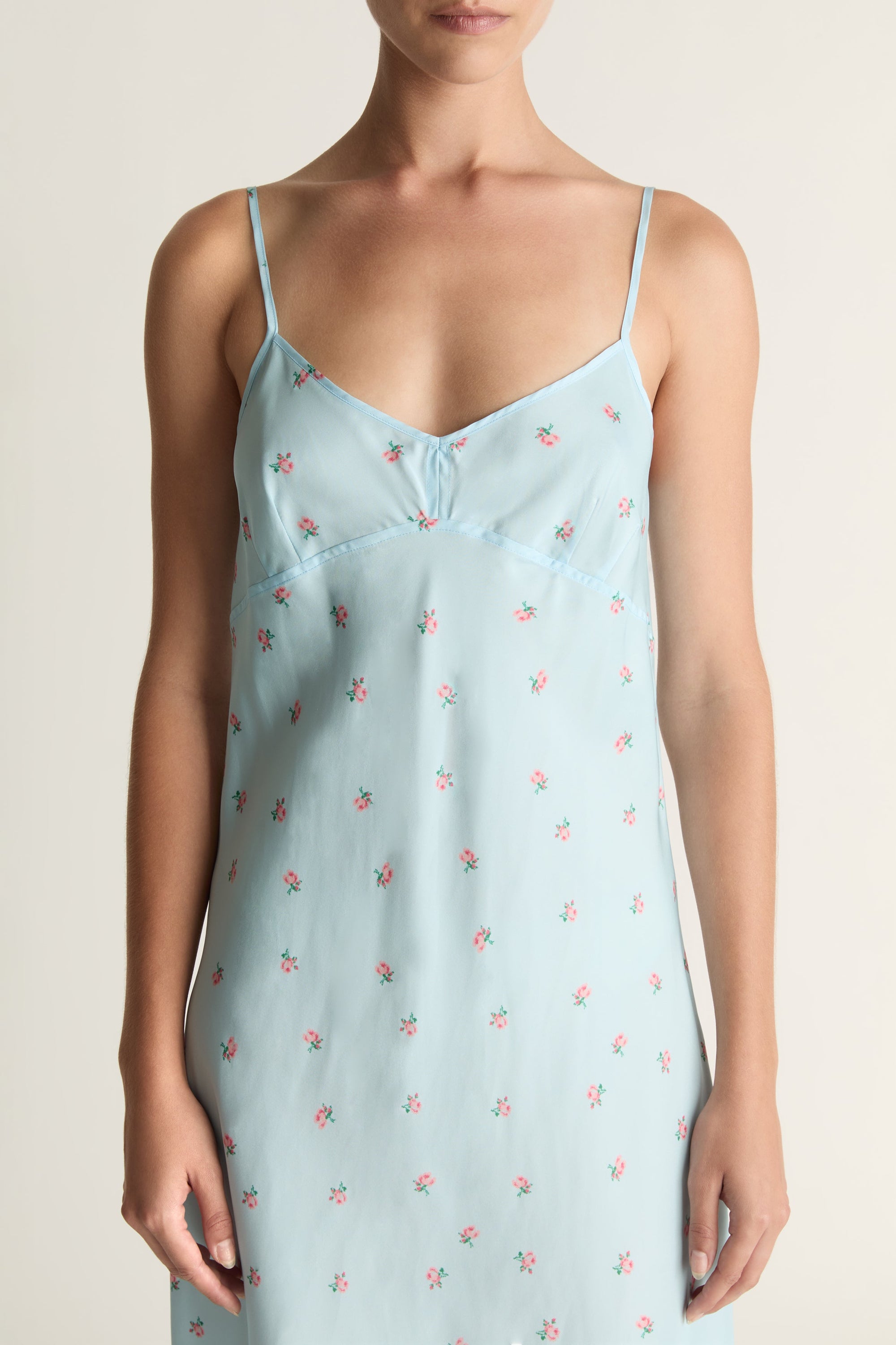 Woman wearing a light blue slip dress with a subtle pattern on a plain background