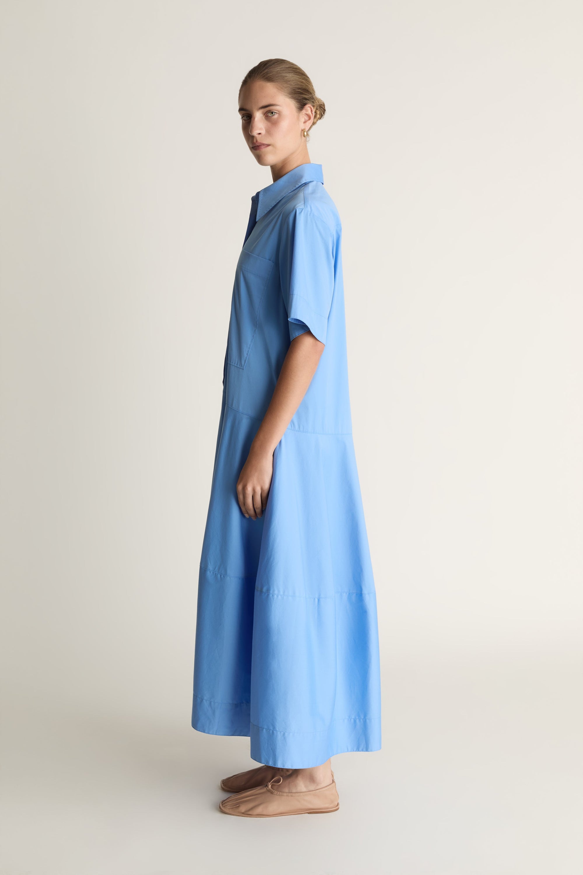 A woman wearing a blue shirt dress against a plain background