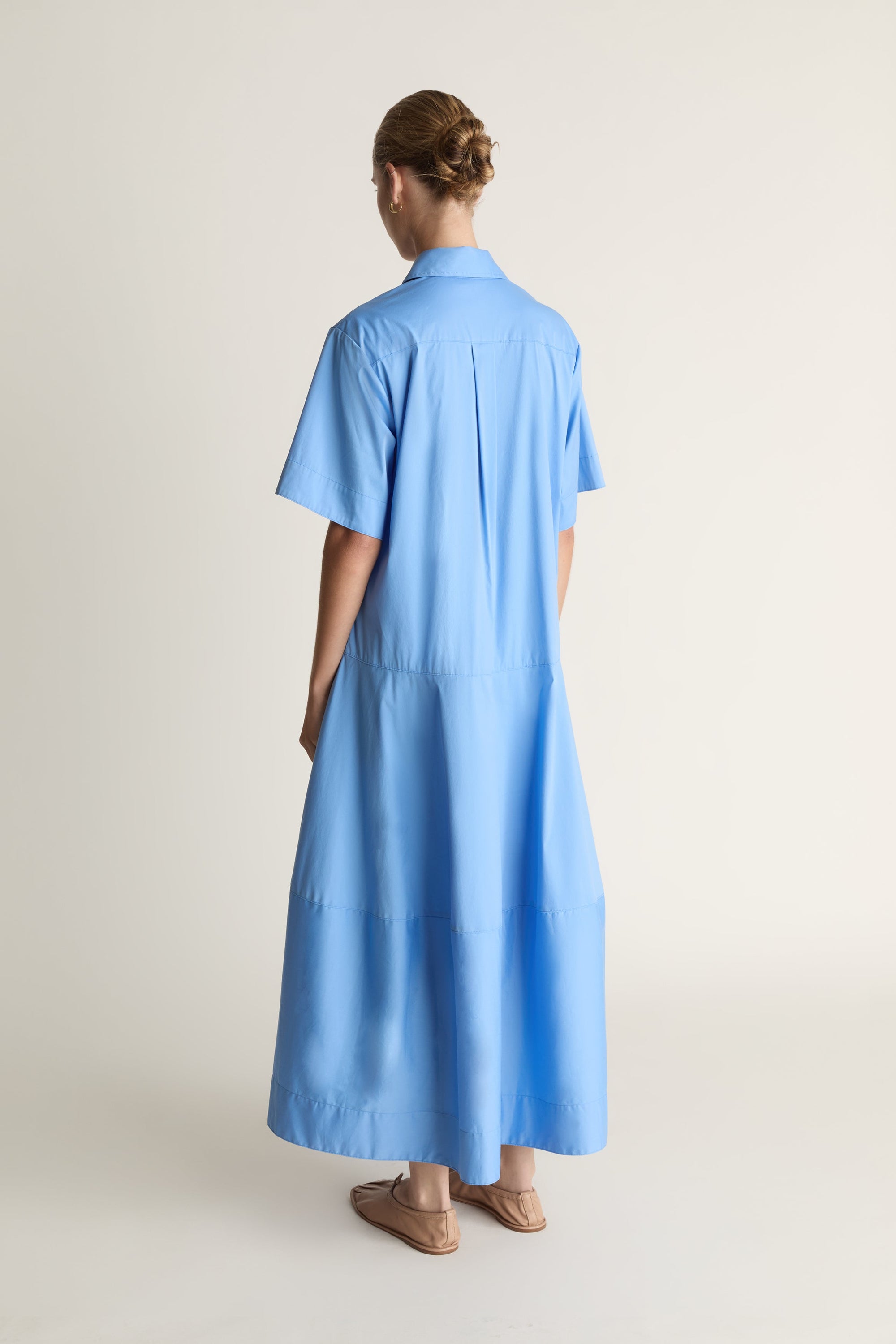 A woman wearing a blue shirt dress against a plain background