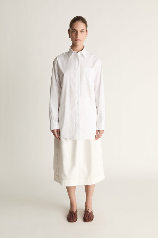 Person wearing a long white shirt and skirt on a plain background