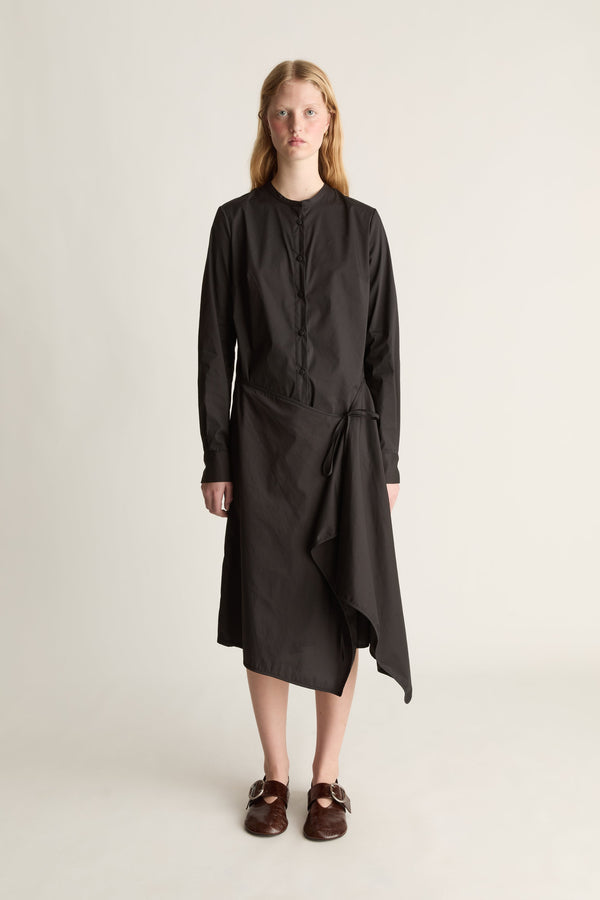 Front view of a woman wearing a long sleeve black cotton midi dress with a wrap detail, shot against a white studio background.