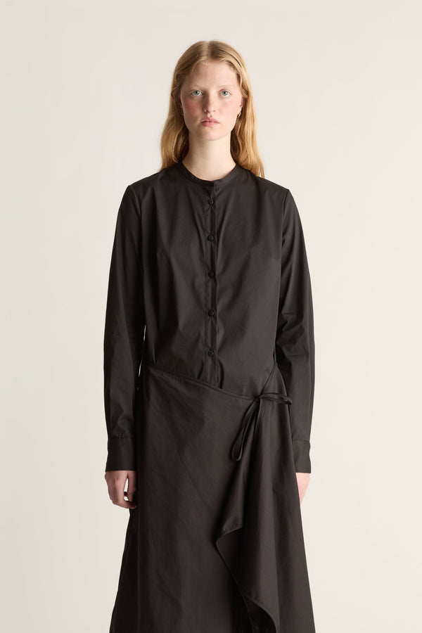Close up of a woman wearing a black cotton long sleeve wrap dress against a white studio background. 