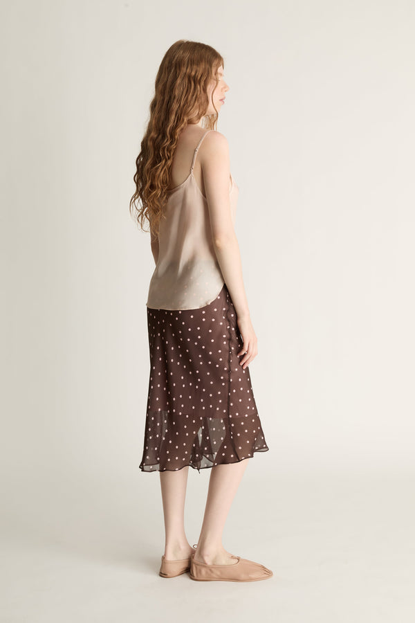 A woman wearing a beige cami top and brown and pink polka dot skirt on a plain background