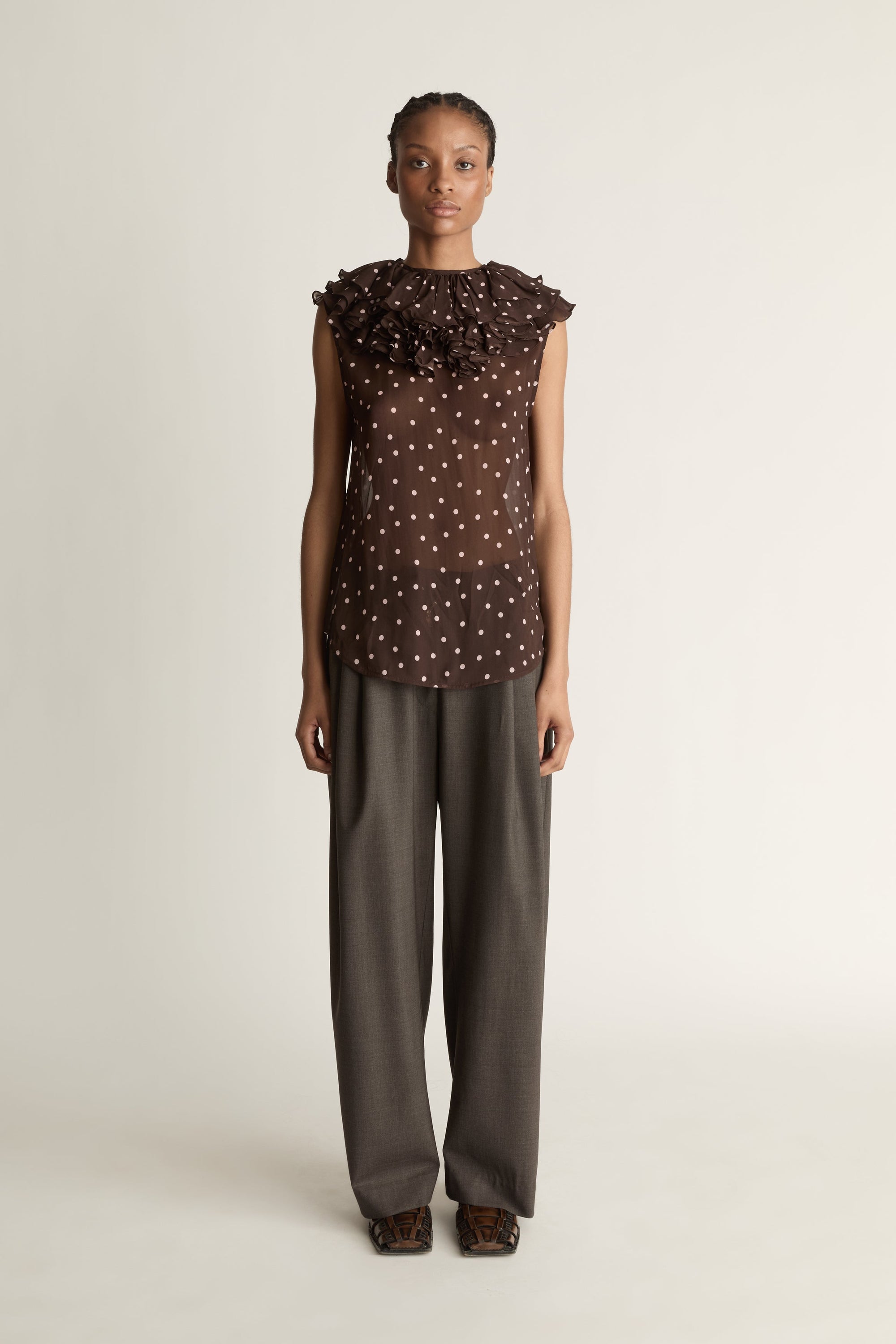 Woman wearing a brown polka dot top and dark pants on a white background