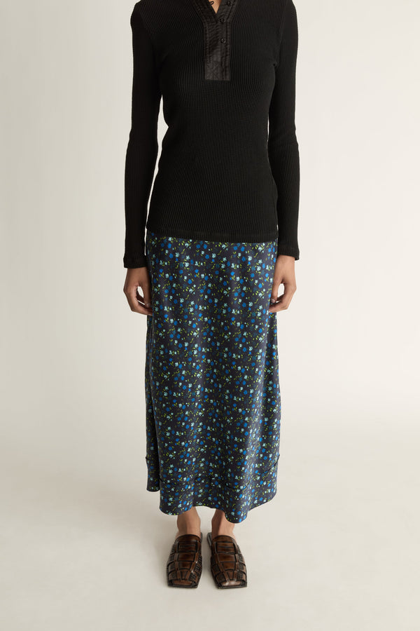 Woman wearing a black long-sleeve top and patterned skirt on a white background