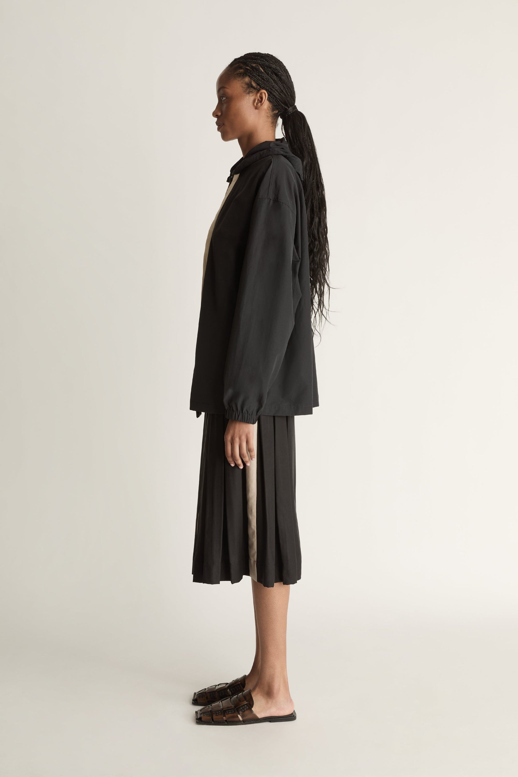 Woman wearing a black jacket with a white zipper and a black pleated skirt on a light background