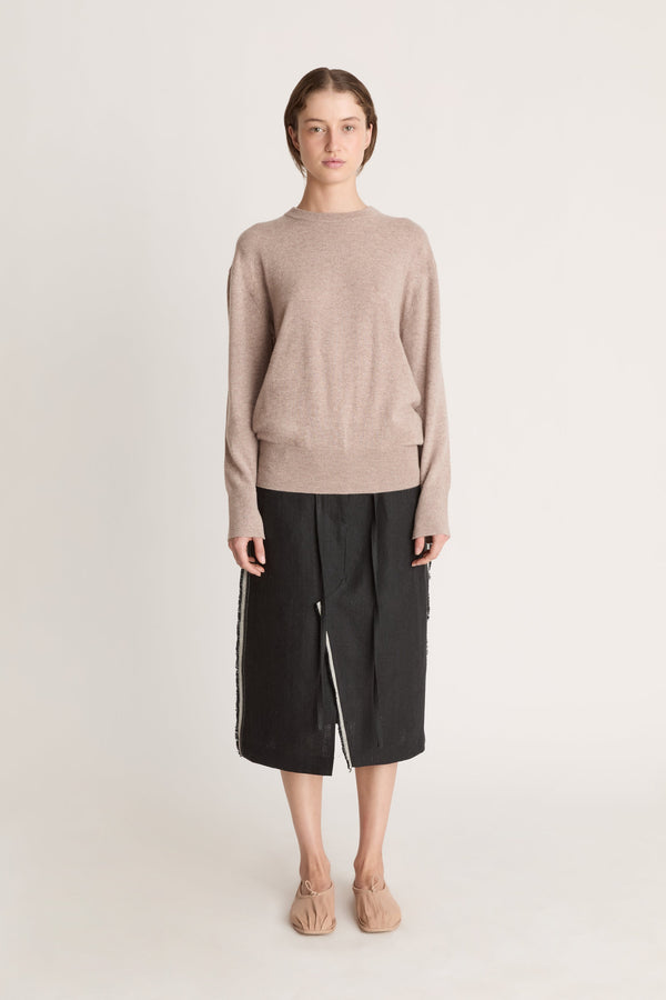 Person wearing a beige sweater and black skirt on a white background