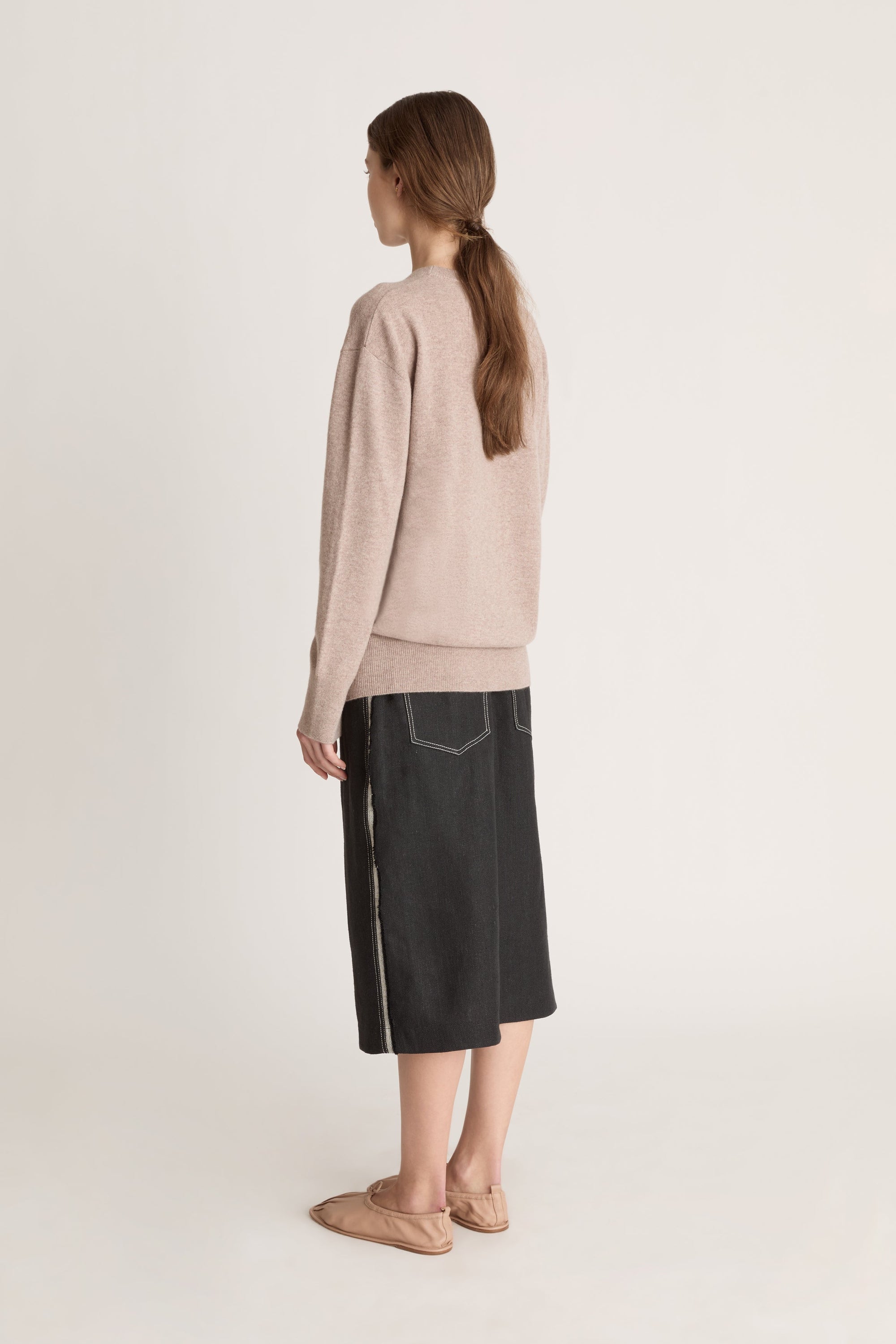 Person wearing a beige sweater and black skirt on a white background