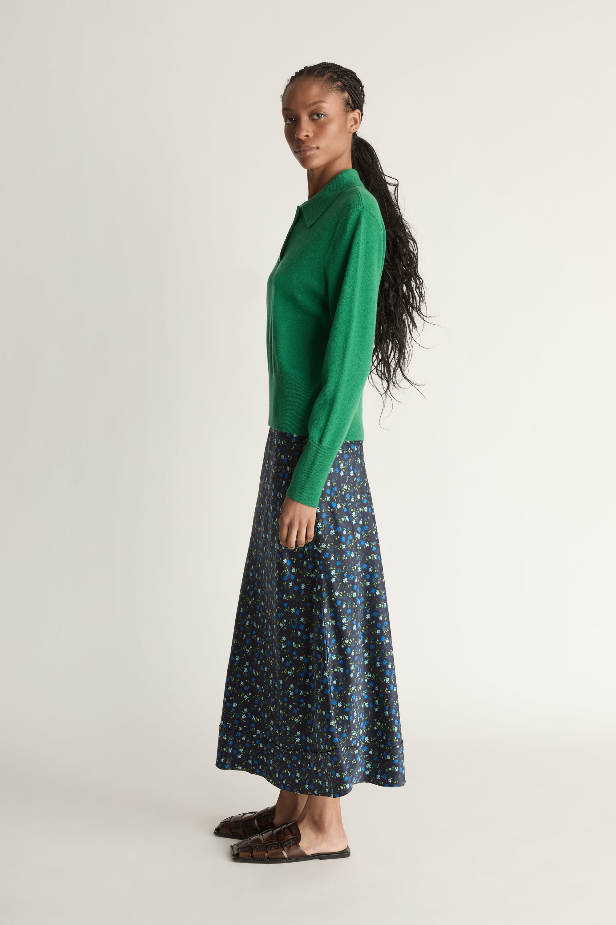 Woman wearing a green sweater and patterned skirt on a white background