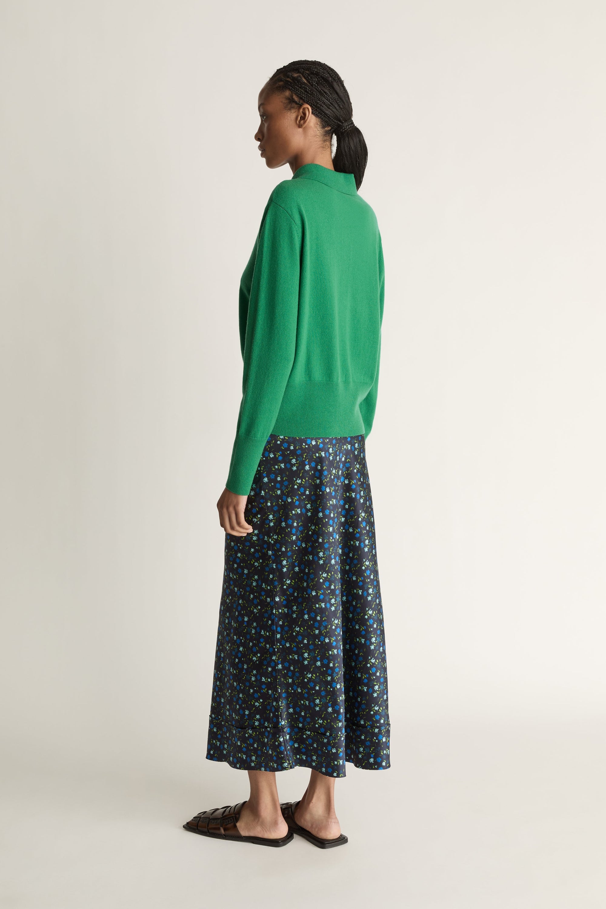 Woman wearing a green sweater and patterned skirt on a white background