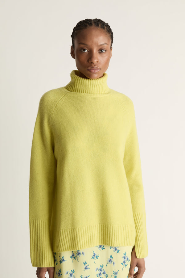 Woman wearing a yellow sweater and floral skirt on a plain background