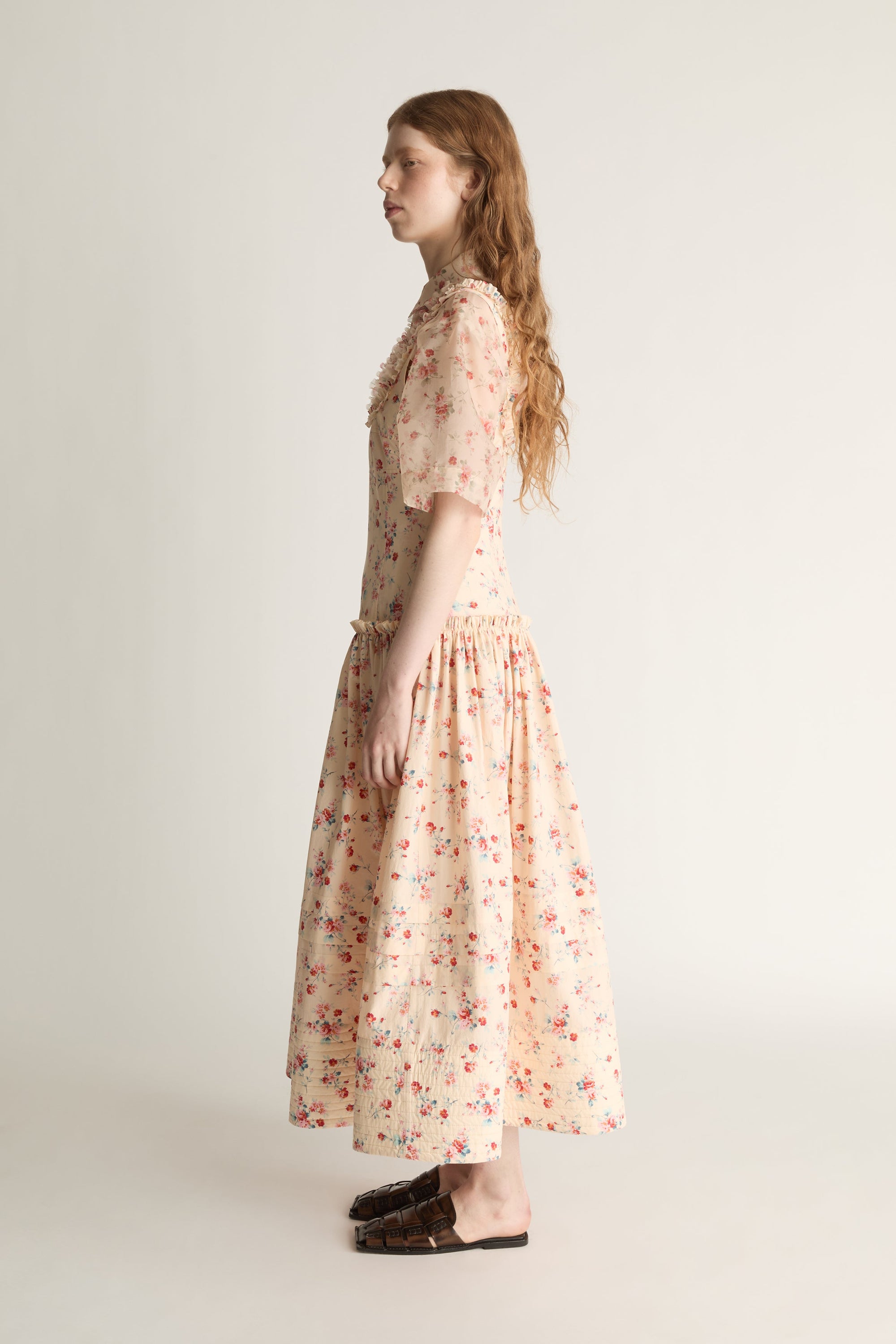 Woman wearing a floral dress over a shirt on a plain background