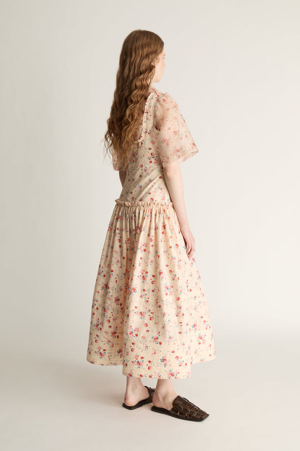 Woman wearing a floral dress over a shirt on a plain background