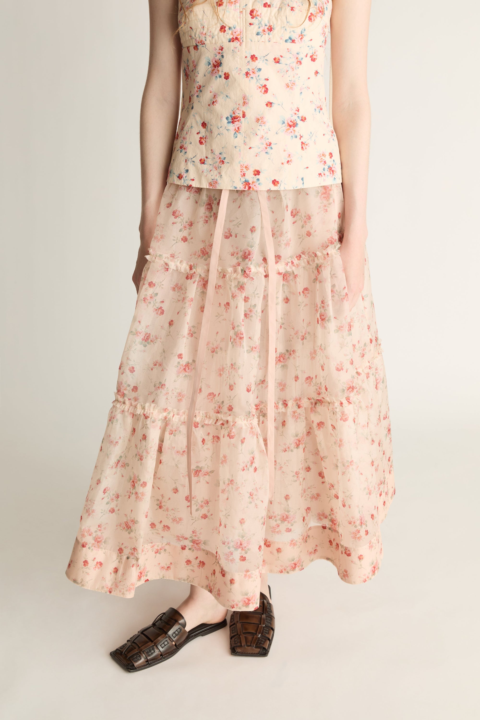 A woman wearing a floral top and skirt on a plain background