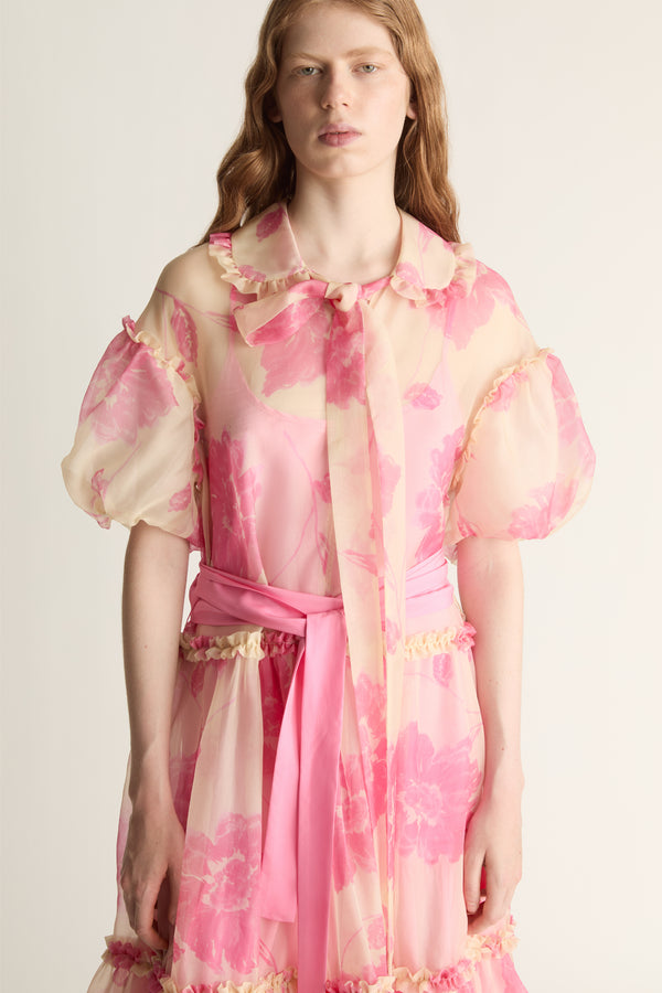 Woman wearing a pink floral dress with puffed sleeves on a plain background