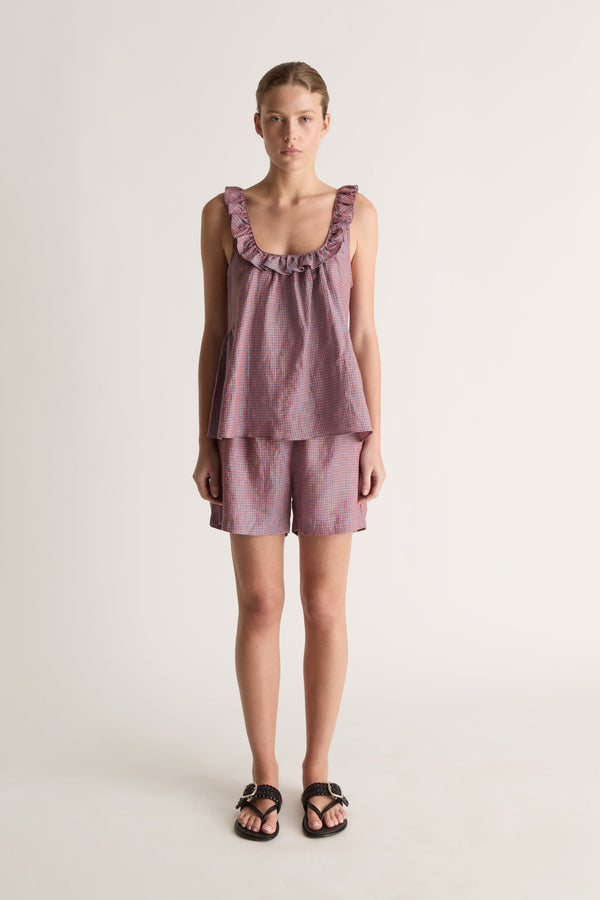 Front view of a woman wearing a plum check ruffle-neck cami top and matching shorts against a white studio background