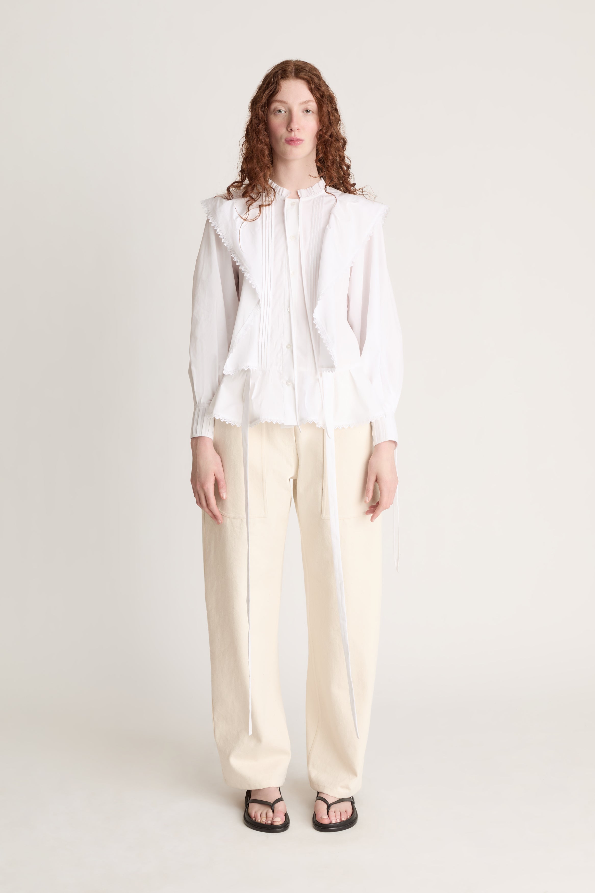 Woman wearing a white blouse and beige pants on a plain background