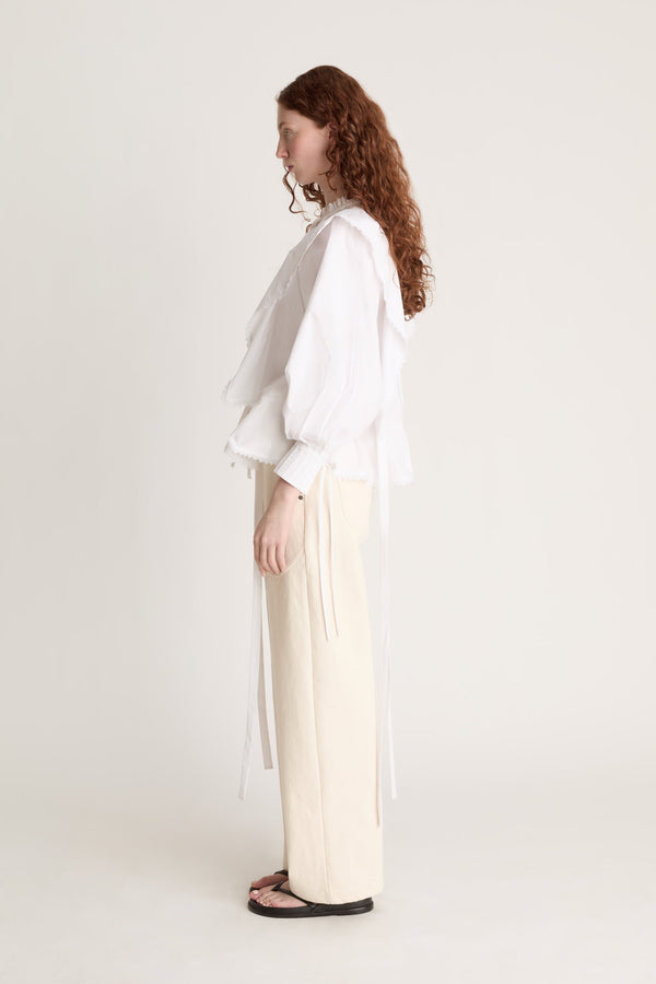 Woman wearing a white blouse and beige pants on a plain background