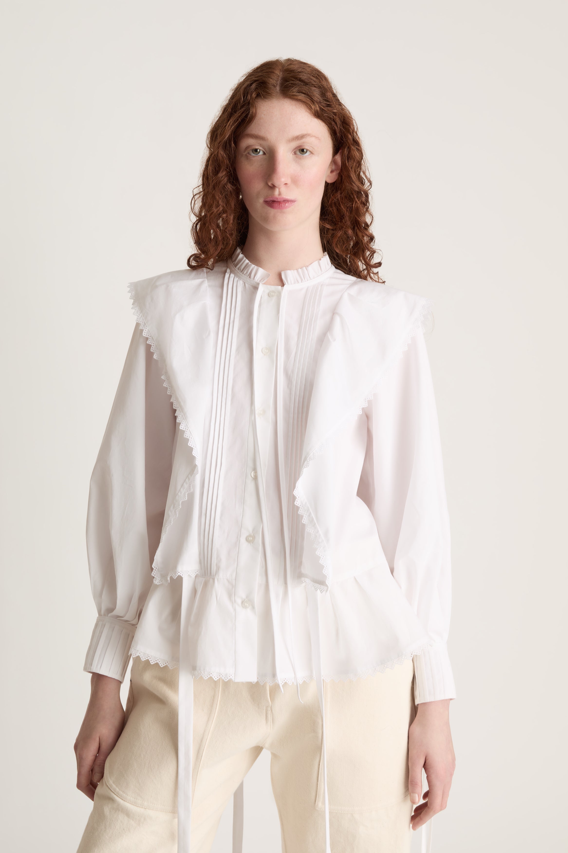 Woman wearing a white blouse and beige pants on a plain background