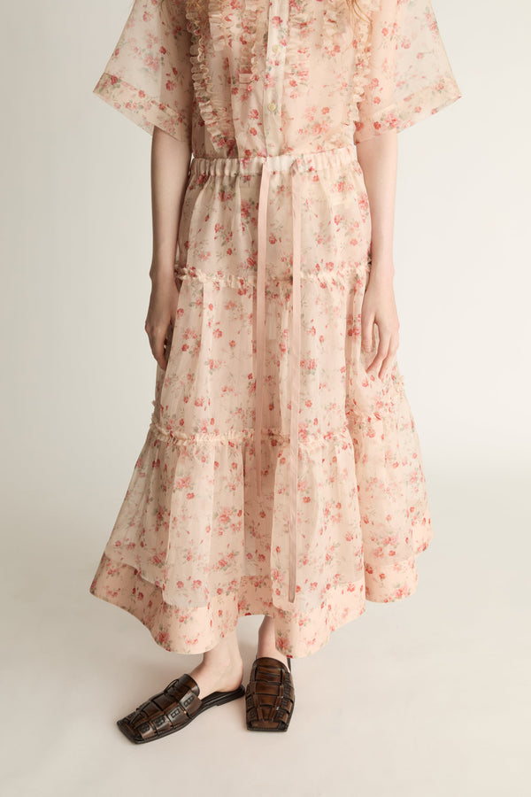 A woman wearing a floral shirt and skirt on a plain background