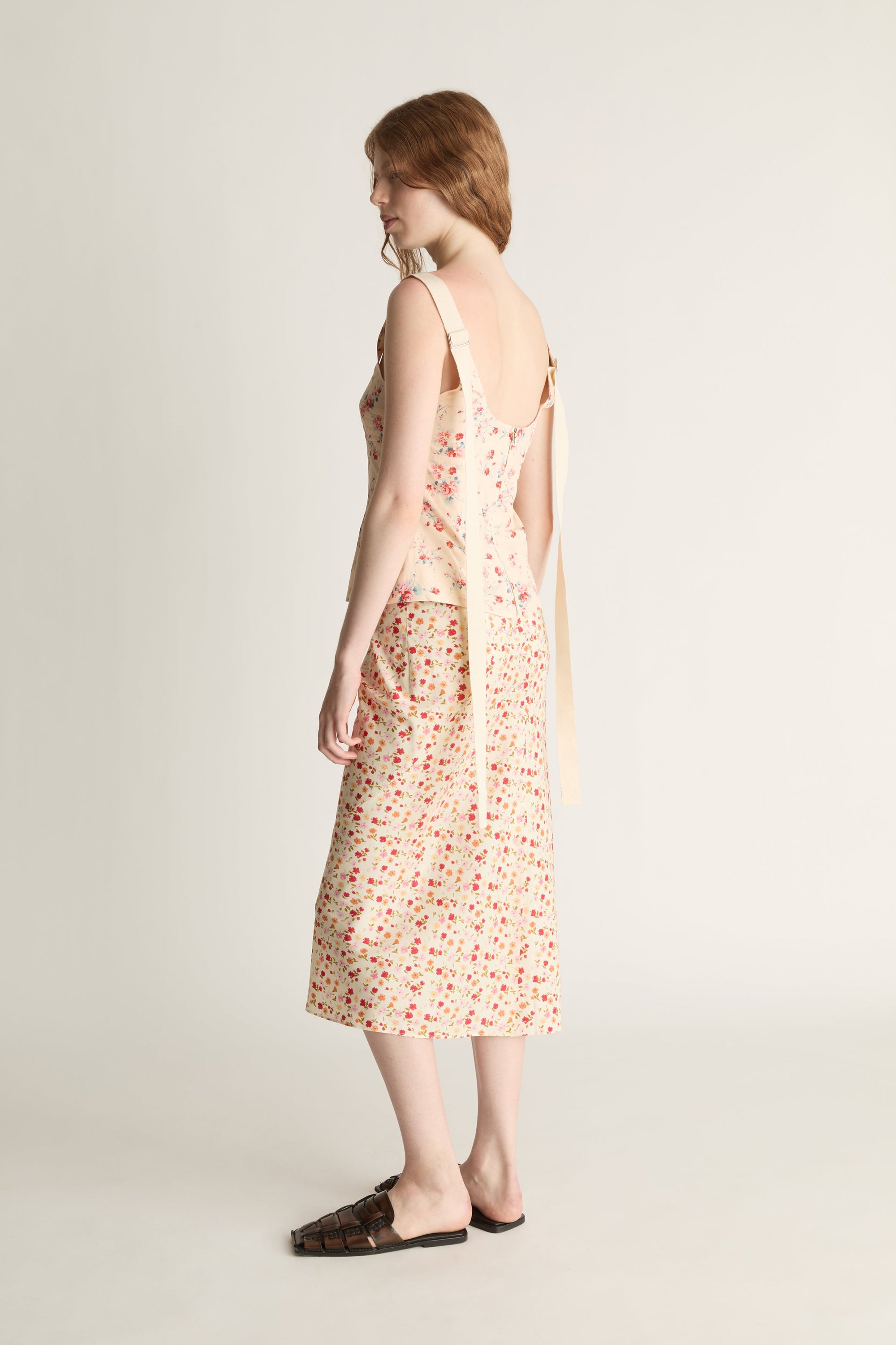 A woman wearing a floral blouse and skirt  on a plain background