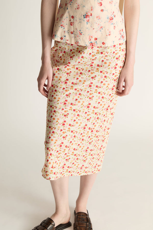 Woman wearing a floral blouse and slip skirt on a plain background