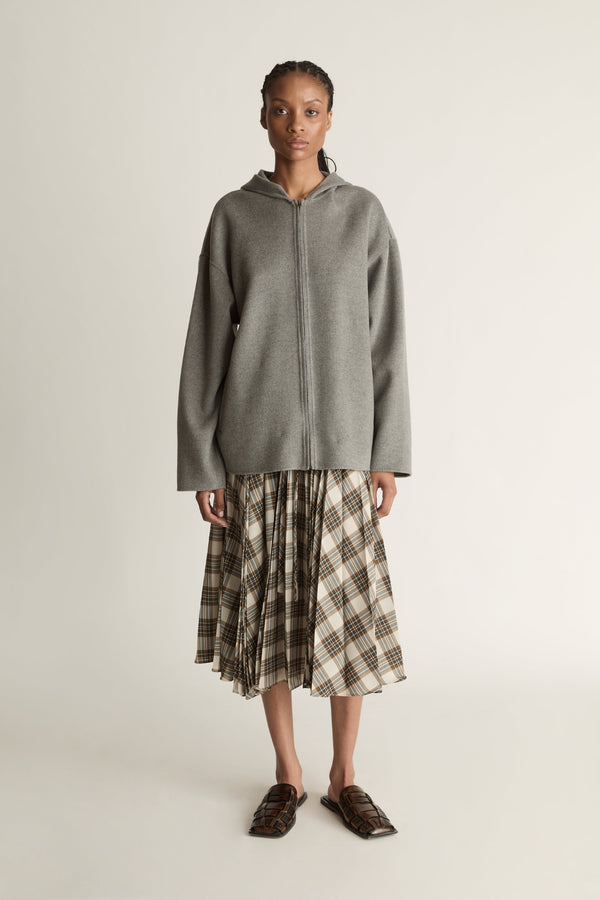 Person wearing a gray hoodie and plaid skirt on a plain background