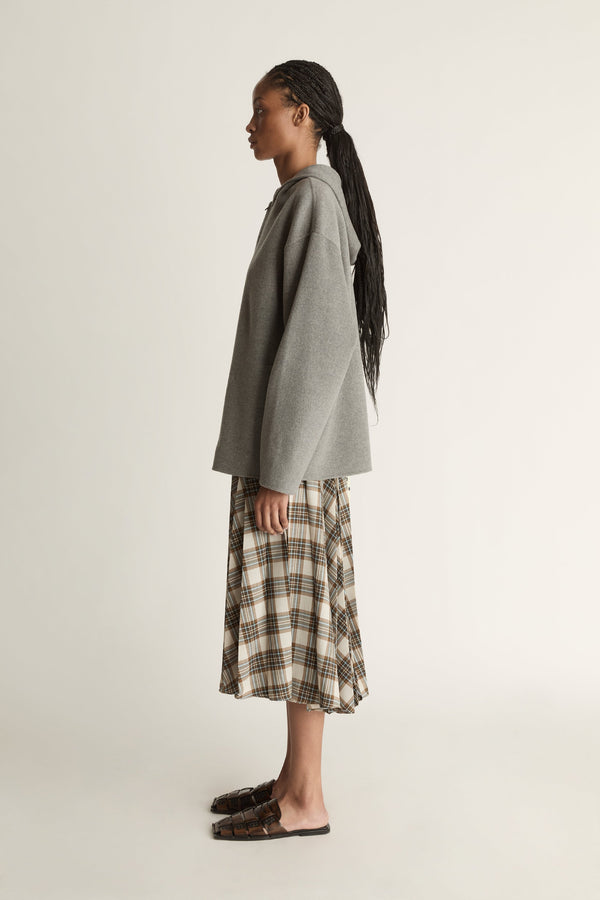 Person wearing a gray hoodie and plaid skirt on a plain background