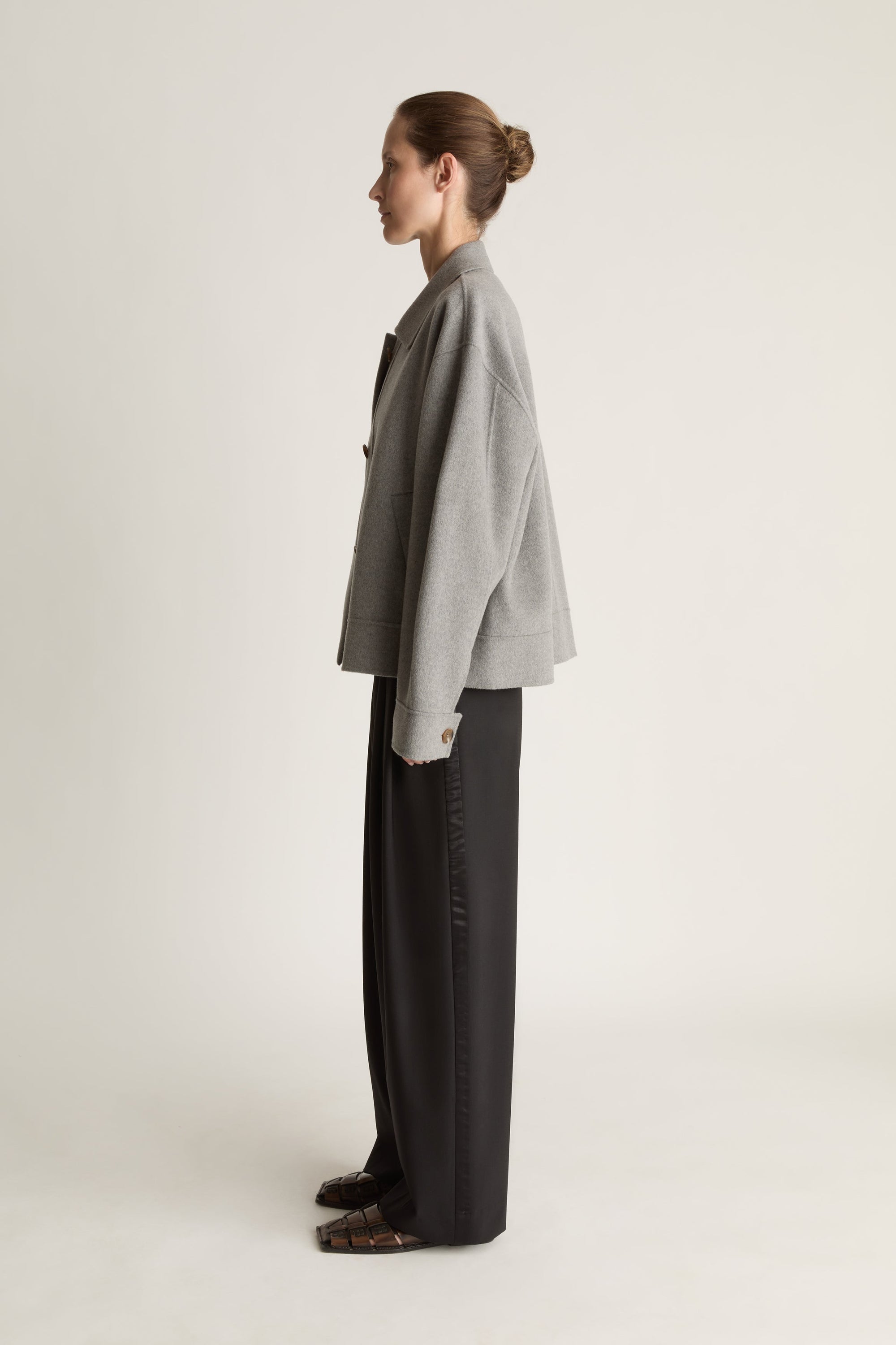 Person wearing a gray jacket and black pants on a white background