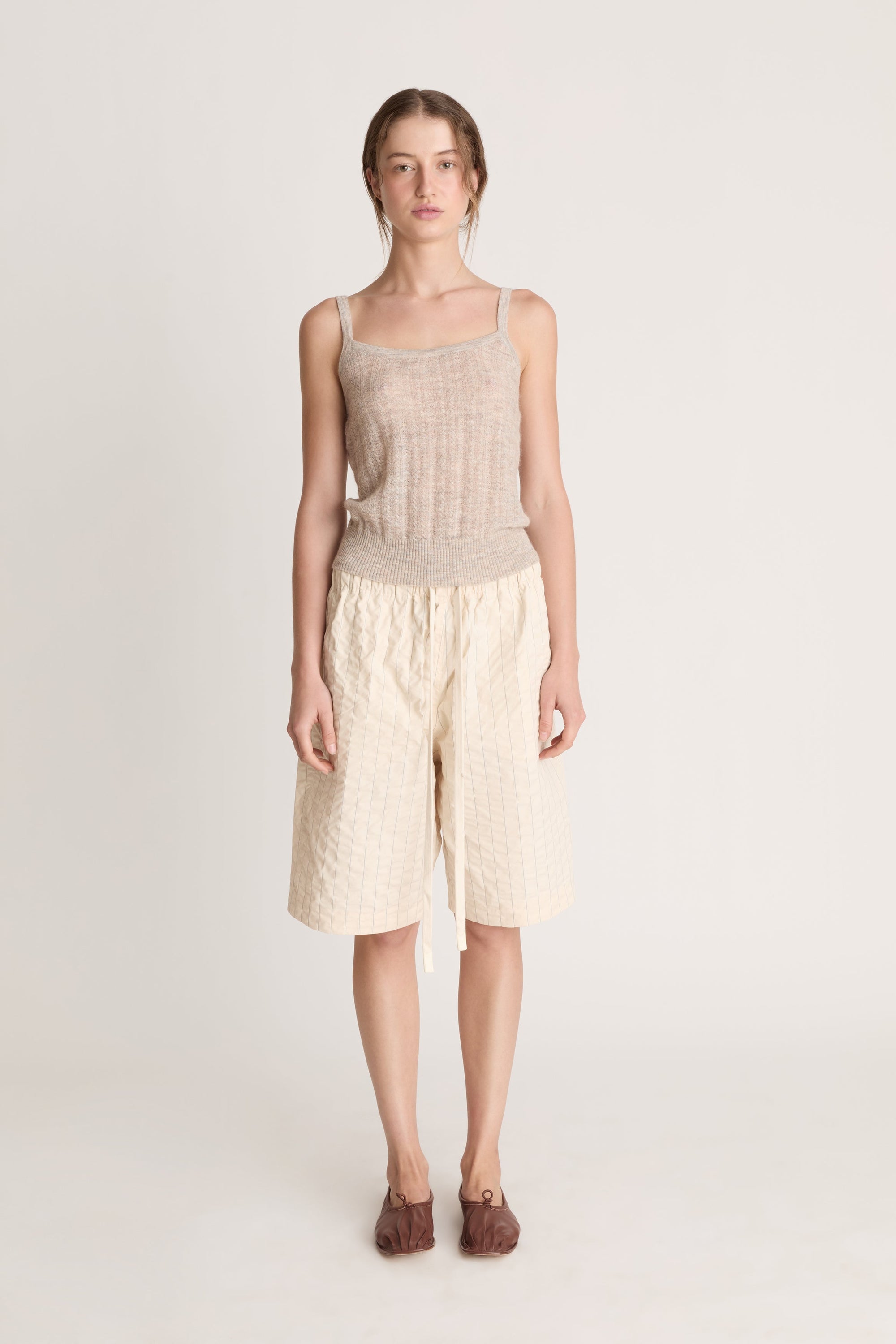 Woman wearing a beige knit cami top and cream coloured shorts on a white background
