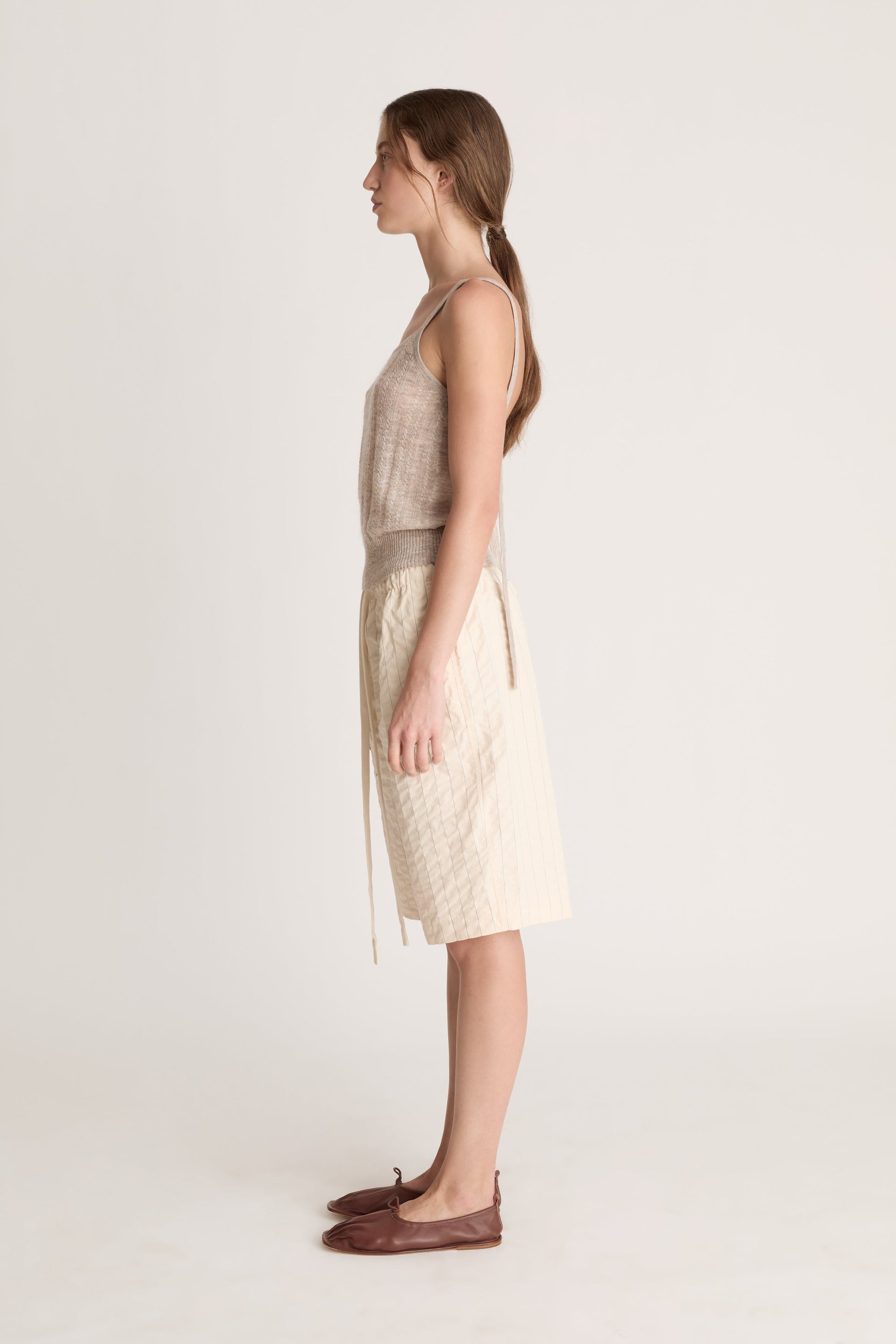 Woman wearing a beige knit cami top and cream coloured shorts on a white background
