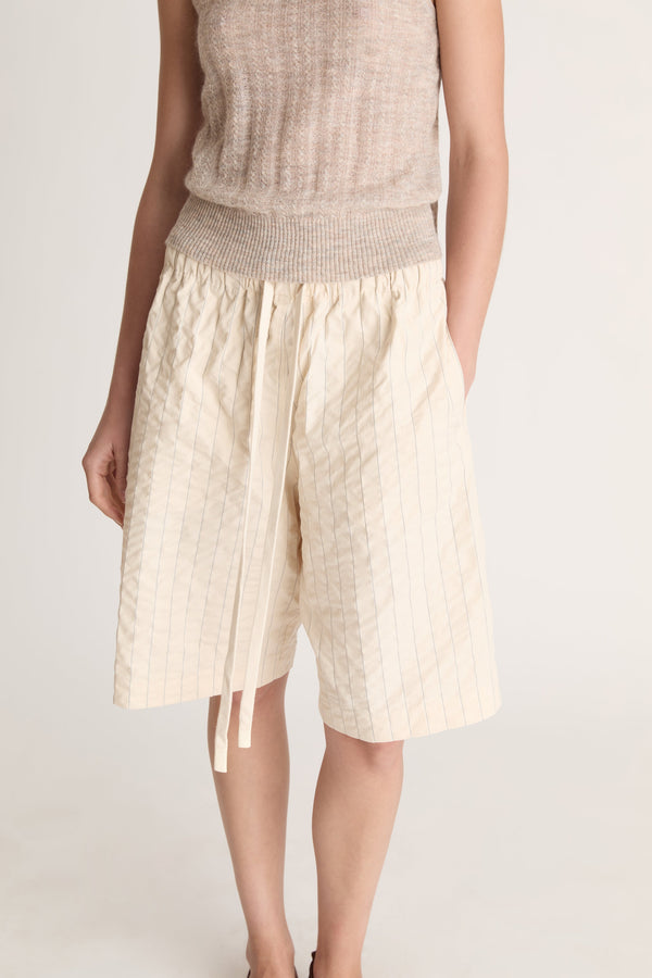Woman wearing a beige knit cami top and cream coloured shorts on a white background