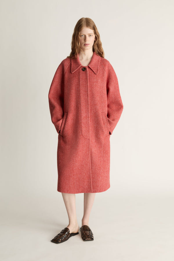 Woman wearing a long red coat on a plain background
