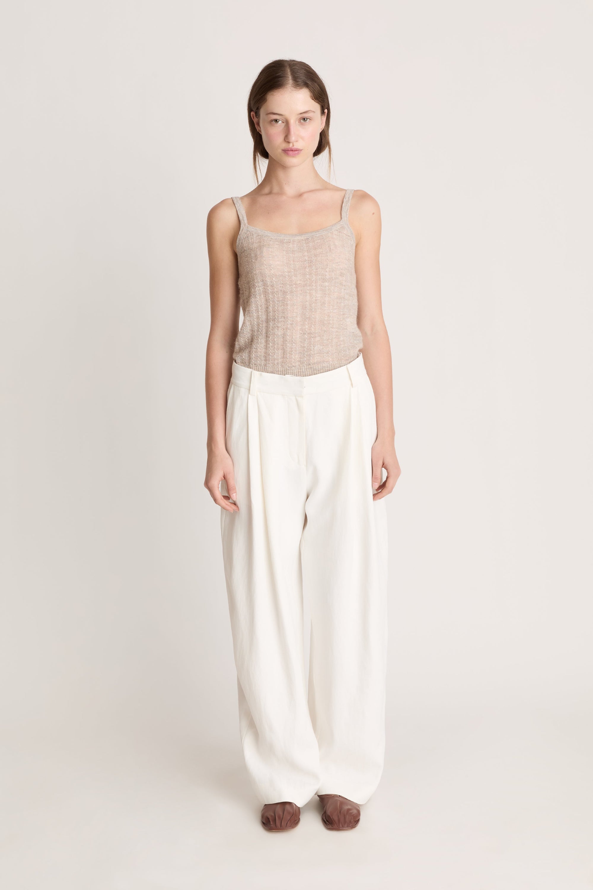 Woman wearing a beige top and white pants on a light background