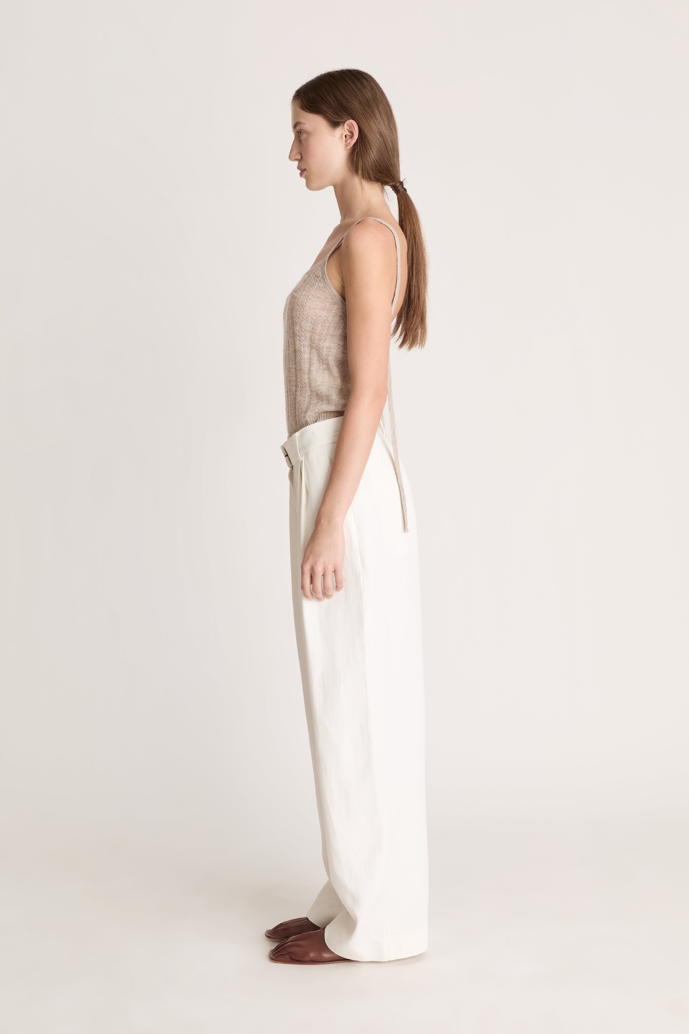 Woman wearing a beige top and white pants on a light background