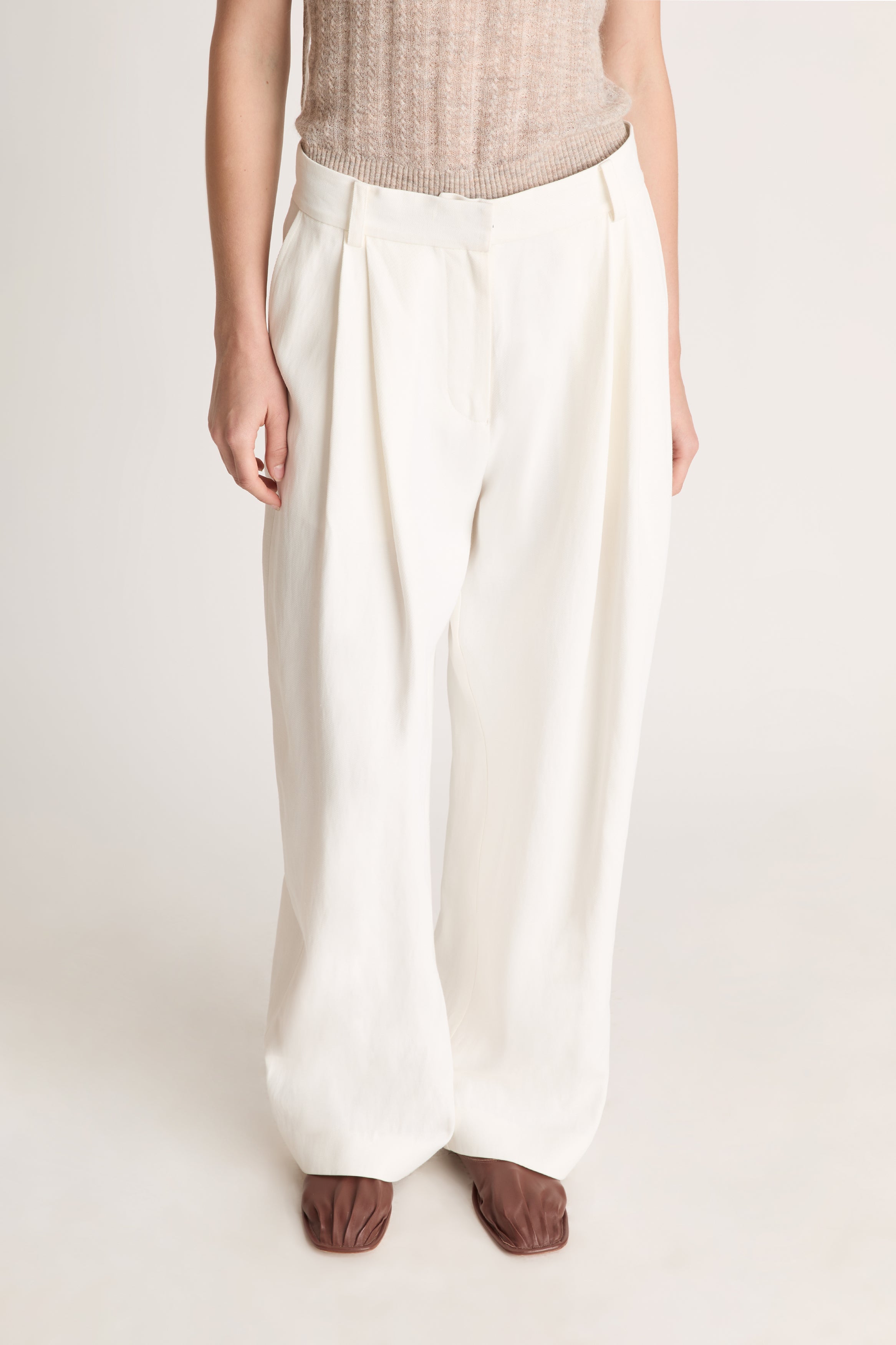 Woman wearing a beige top and white pants on a light background