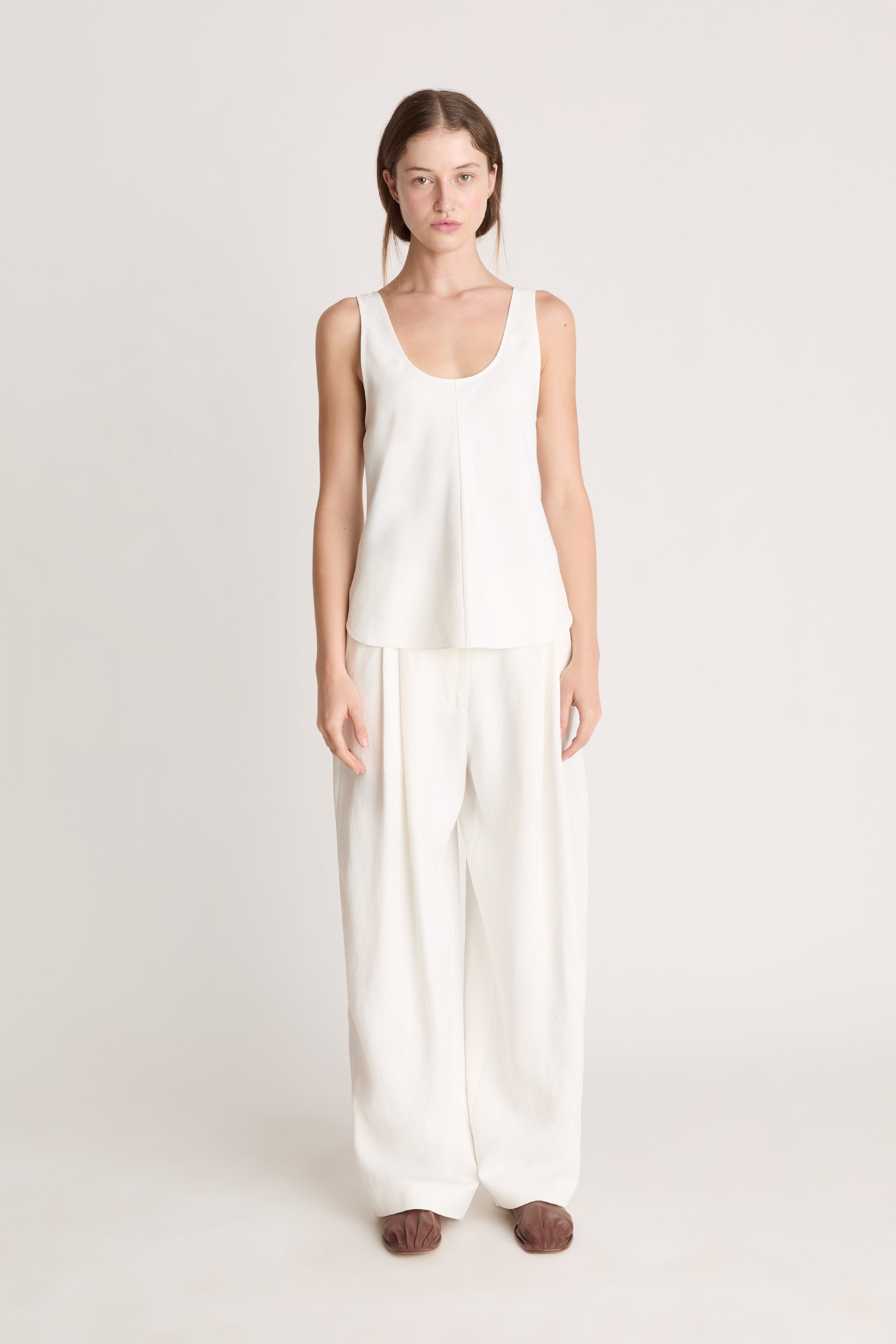 Woman wearing a white tank  top and white trousers on a white background