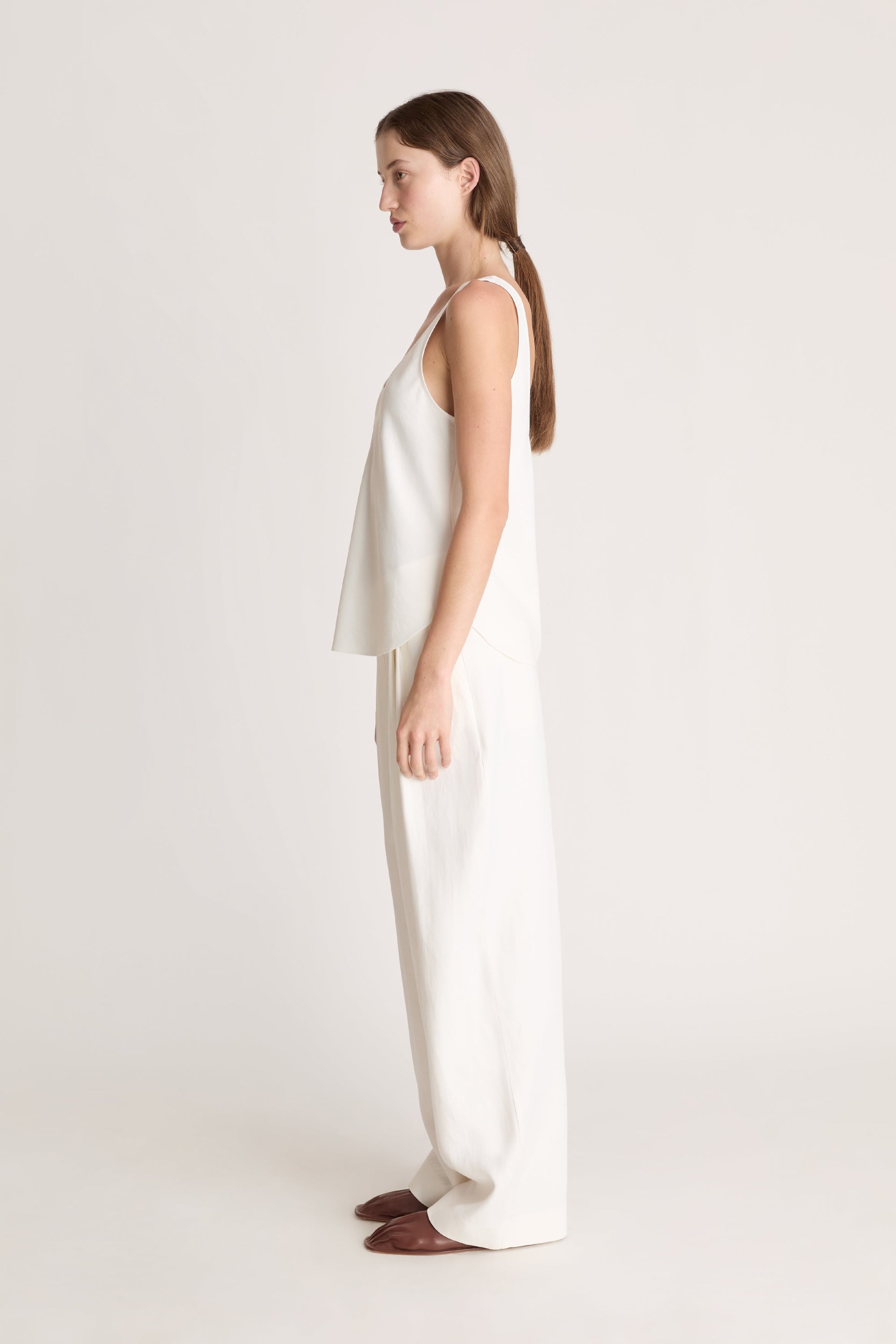 Woman wearing a white tank  top and white trousers on a white background