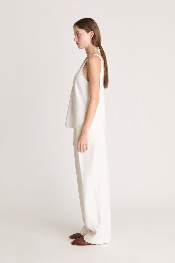 Woman wearing a white tank  top and white trousers on a white background