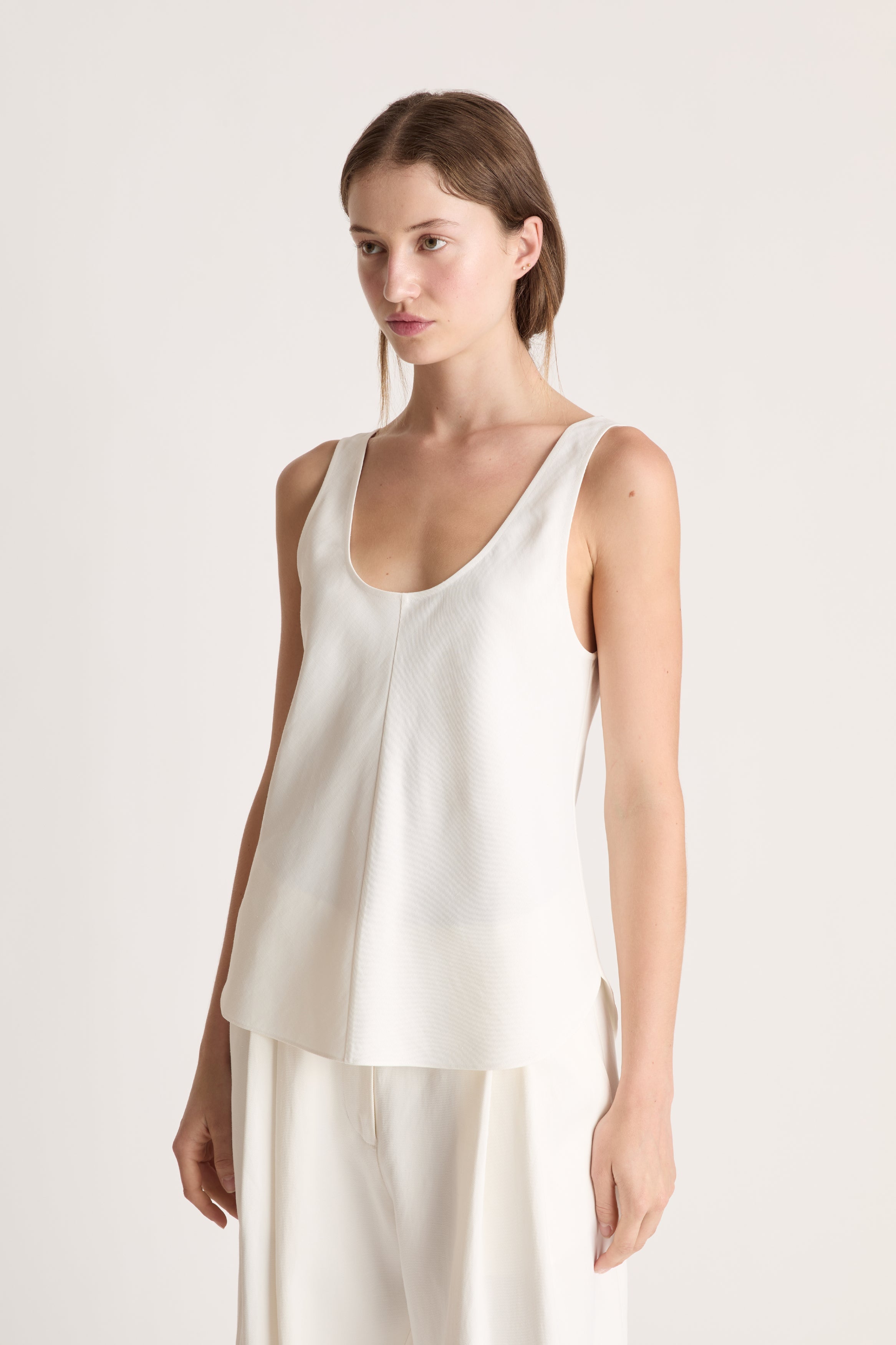 Woman wearing a white tank  top and white trousers on a white background