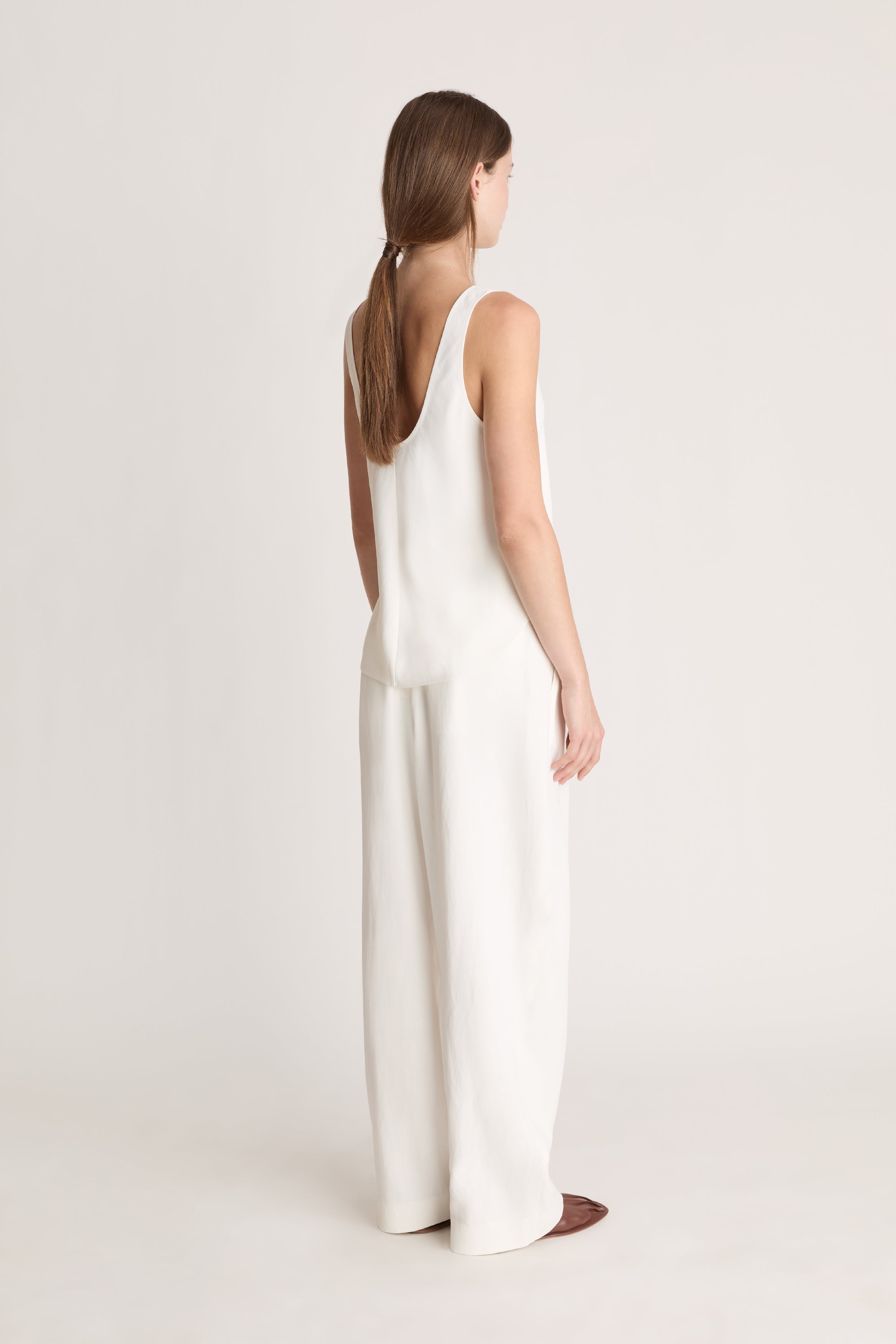 Woman wearing a white tank  top and white trousers on a white background